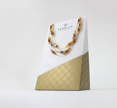 Una collana Rebollo di cristalli ambrati su un espositore geometrico di colori bianco e oro. Sfondo neutrale.