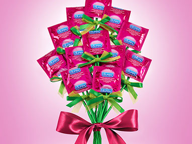Un bouquet di fiori creato con i preservativi Durex nelle confezioni di colore rosa. Grande fiocco rosa sugli steli. Sfondo Rosa. Scherzoso.