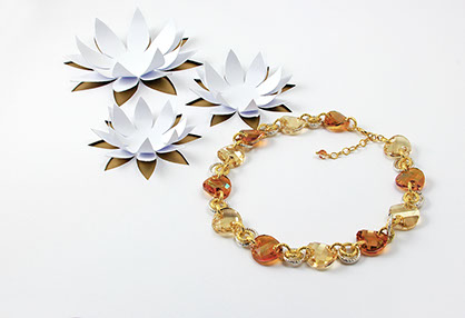 Collana Rebollo di cristalli ambrati. Vicino tre fiori di loto ritagliati dalla base di carta bianca. Sotto i fiori si intravede la carta dorata