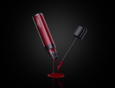 Un lip gloss. Il liquido rosso scorre via dalla confezione capovolta. La punta del pennello con una goccia. Sfondo nero con la luce centrale.