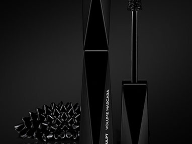 Una mascara della Kiko di forma geometrica, nera. Sulla sinistra il ferrofluid a forma di un riccio nero e lucido. Sfondo nero. Verticale.