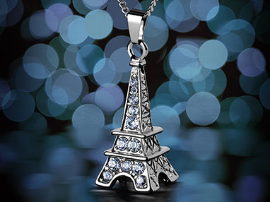 Un ciondolo a forma della Torre di Eiffel con i cristalli azzurri sulla catena. Sfondo scuro con i bokeh blu e azzurri. Verticale.