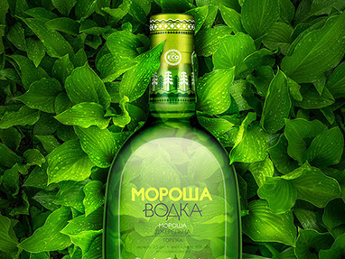 A bottle of vodka on the background of green leaves. The light warm light illuminates the leaves around from the inside of the bottle.
