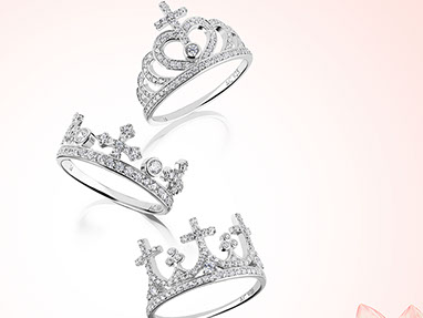 Three silver rings with crystals, with the shape of the crown with crosses. White-pink background and a pink flower in the bottom right corner. 