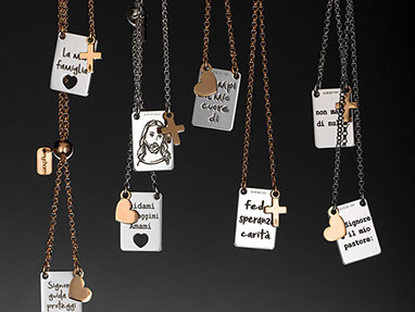 Religious necklaces by Mycharm with chains, silver rectangular pendants and little gold hearts and crosses. Black background.