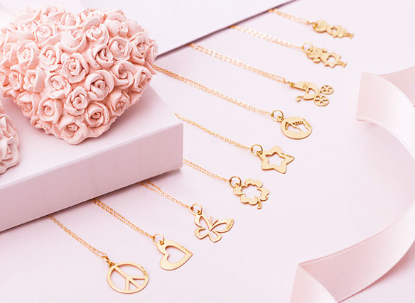 Una composizione di 9 medagliette d'oro con le catenine Mycharm. A sinistra cuori di gesso, a destra un nastro. Tutto in tinte rosa e oro.